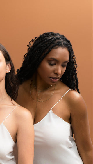 Three women wearing white slip dresses standing next to a mannequin also wearing a white slip dress against a brown background.